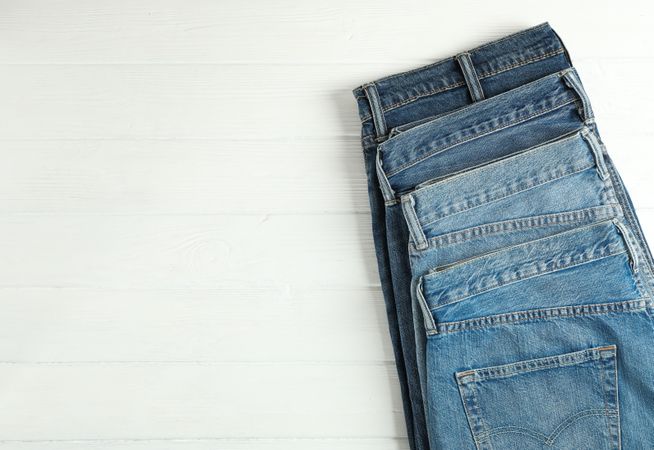Different jeans folded on a wooden background, space for text