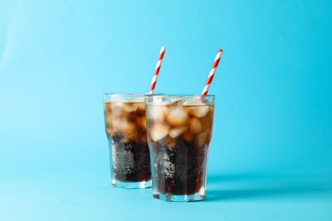 Glasses with cold cola and tubule on blue background, space for text