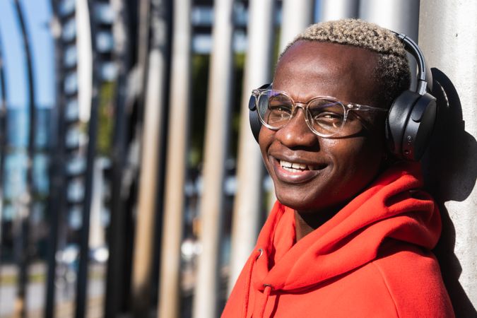 Cheerful Black male listening to music in headphones while chilling in park
