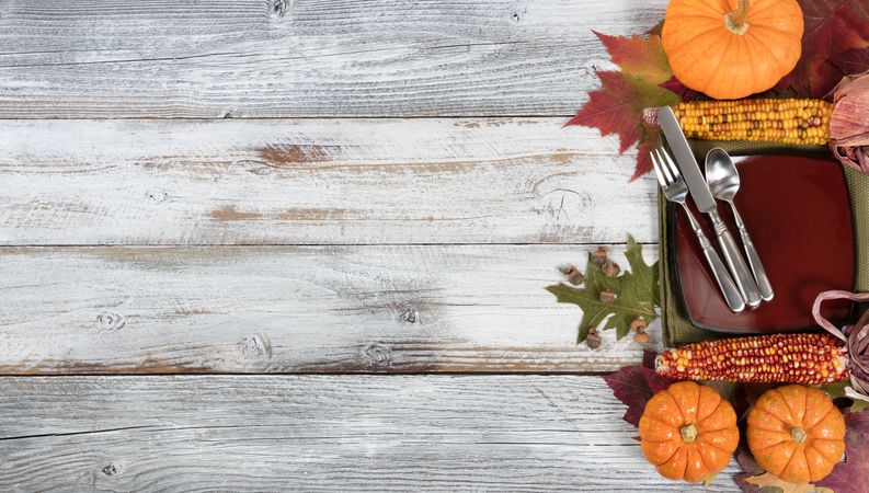 Basic dinner setting with autumn foliage and other fall decorations on rustic wooden boards