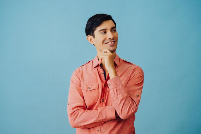 Mid portrait of curious Hispanic male smiling while looking away from camera