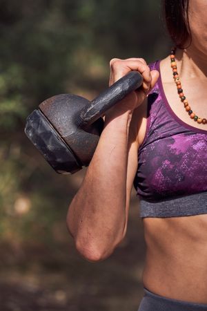 Faceless sportswoman lifting kettlebell in nature