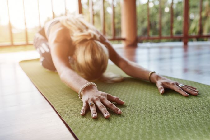 Woman stretching forward, performing a yoga pose on exercise mat