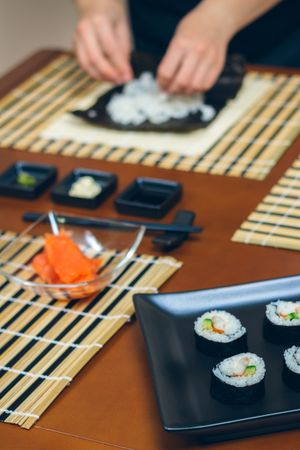 Chef preparing sushi with plate of finished maki rolls, vertical