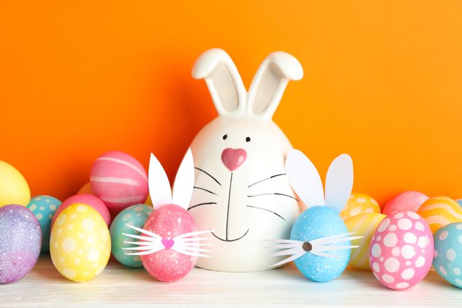 Decorated bunny and Easter eggs on table against color background. Space for text