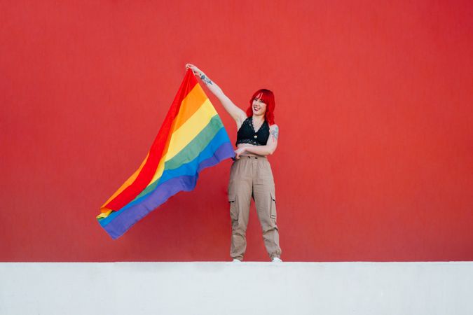 Young woman holding rainbow flag standing against red background