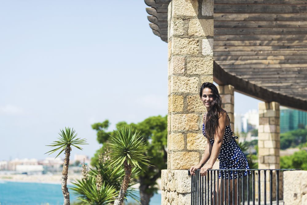 Beautiful hispanic woman in blue dress leaning over rail at view