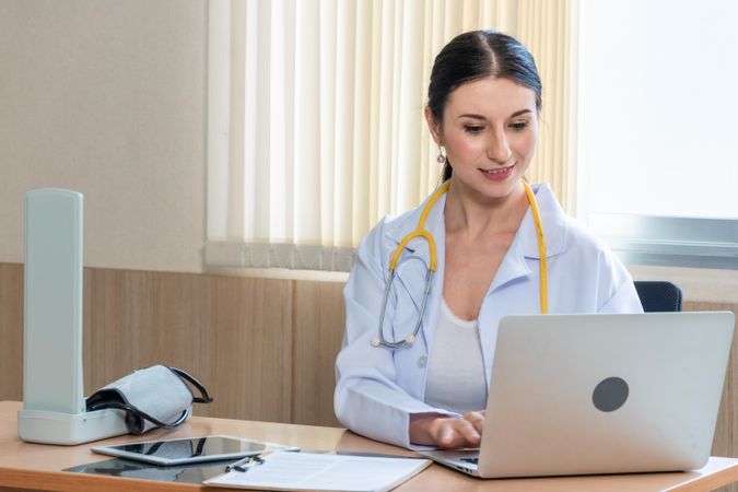 Medical professional sitting in her office reviewing notes on laptop