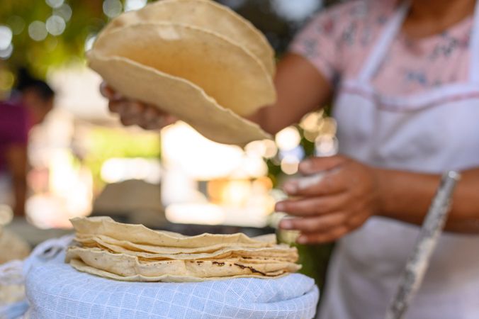 Unrecognizable woman forming heap of tortillas in nature