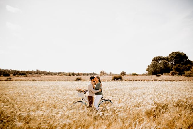 Sincere lovers posing by bicycle on rye field