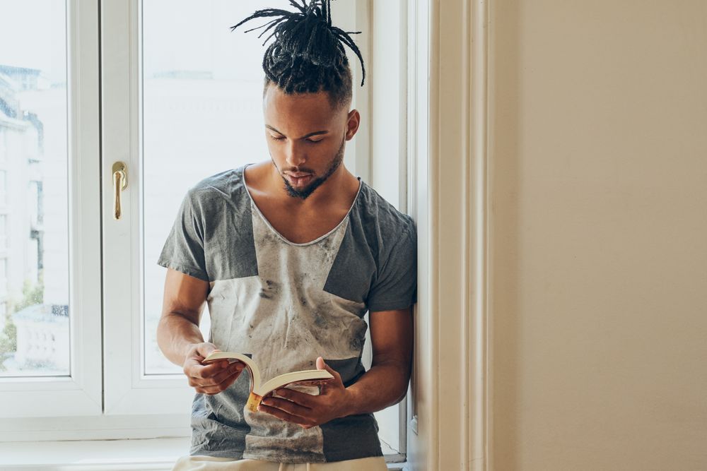 Black male standing by window and reading