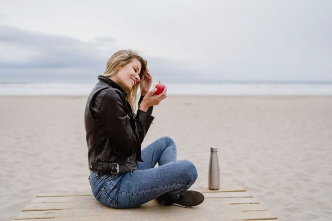 Woman eating an apple sitting on beach