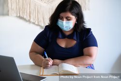 Woman in medical face mask writing notes in a bright modern office 43lRXb