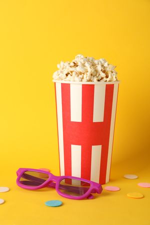 Striped bucket with popcorn and 3d glasses on yellow background, copy space
