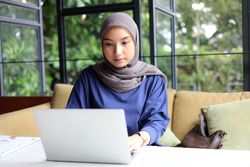 Asian Muslim Woman in Hijab Working Online at Cafe, using Laptop and Drinking Coffee or Tea.