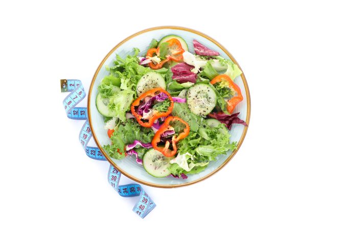 Plate with fresh salad and measuring tape isolated on plain background