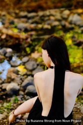 Back view of woman in dress sitting by a creek in nature 4BaQk5