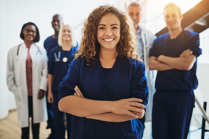 Smiling doctor with arms folded and staff behind her