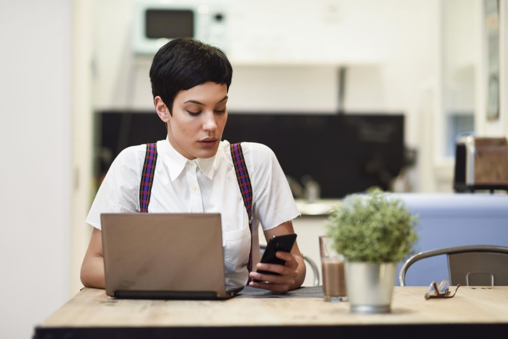 Woman in loft apartment checking her smart phone while working at home