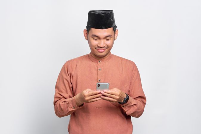 Muslim man in kufi hat smiling looking down at smart phone