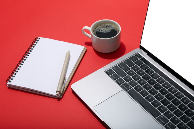 Top view of laptop keyboard with mockup screen on red table with coffee and notebook