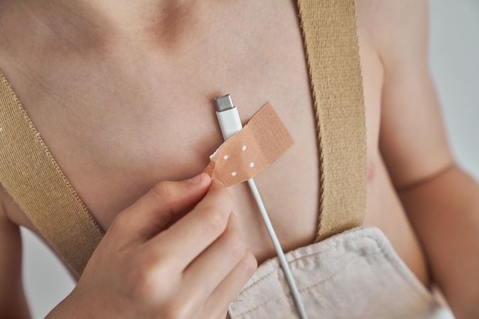Unrecognizable boy gluing phone charger on chest with plaster