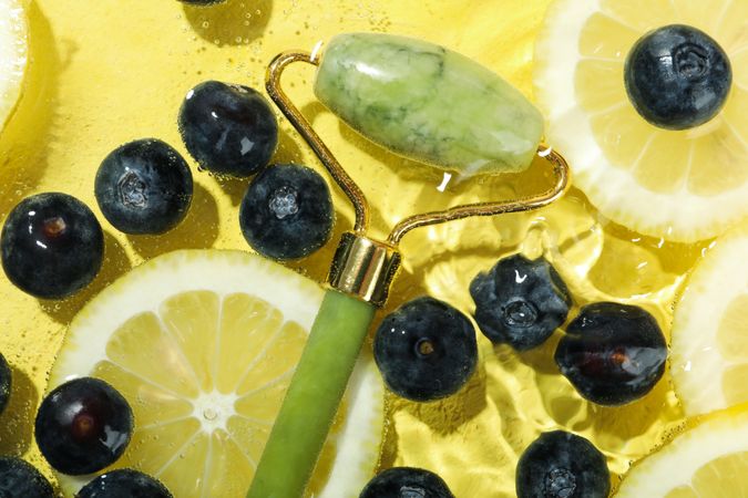 Top view of blueberries and lemons soaking in water with jade roller