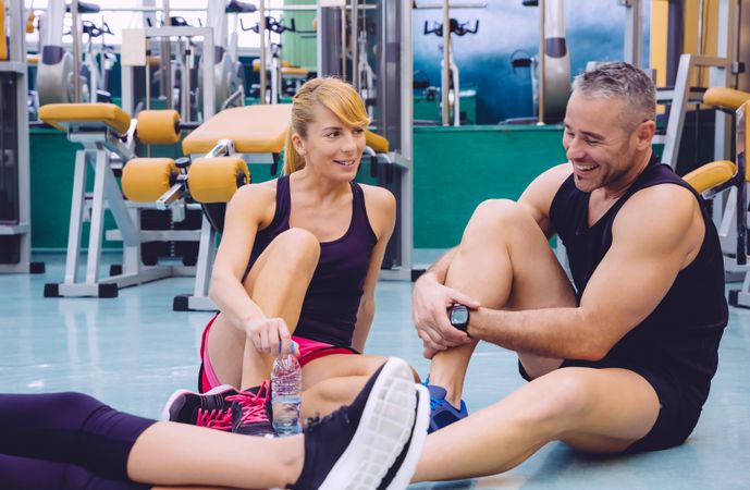 Man and woman sitting on gym floor after workout