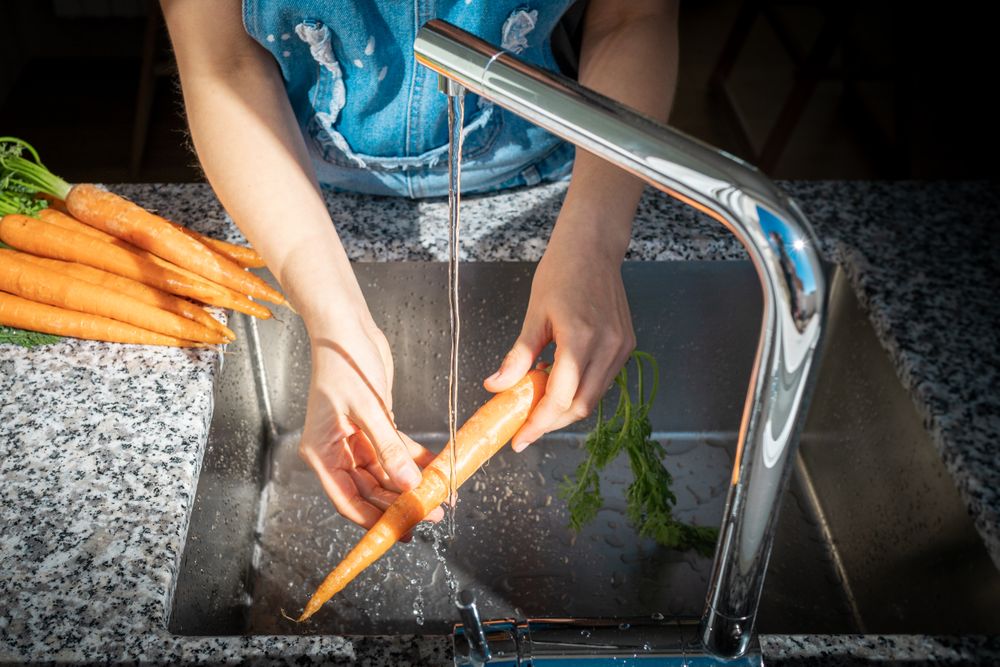 Crop woman hands washing carrot