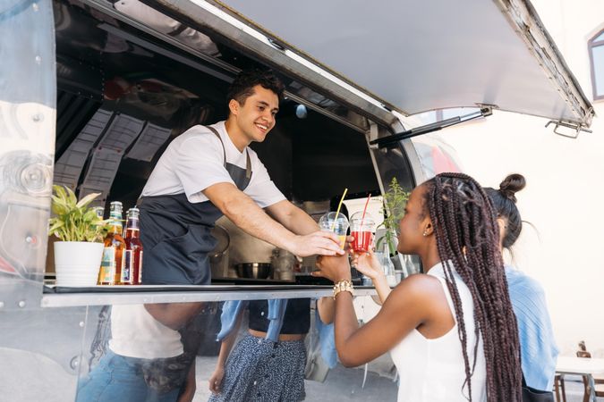 Cheerful salesman in apron handing drinks to female clients