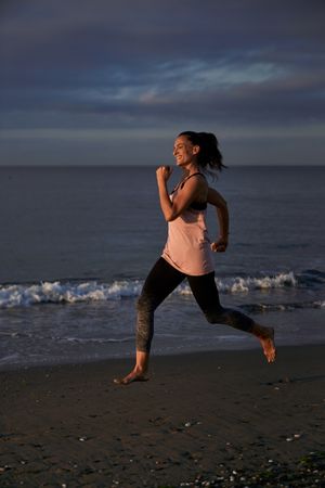 Content Hispanic woman running on sandy shore