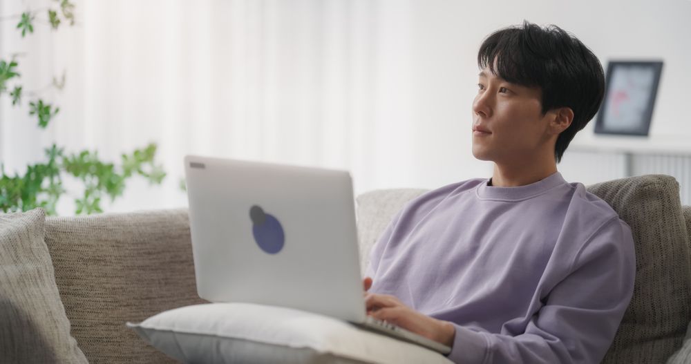 Young Asian Male Browsing Internet, Using Laptop Computer at Home