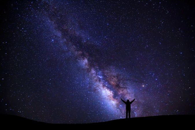 landscape with milky way, Night sky with stars and silhouette of a standing sporty man with raised up arms on high mountain.