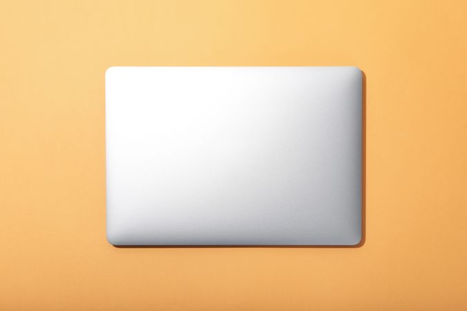 Top view of closed laptop on light orange desk