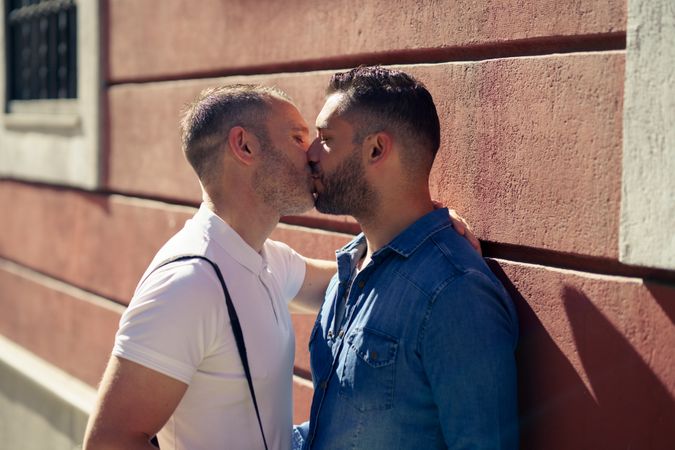 Two men kissing beside wall outdoor
