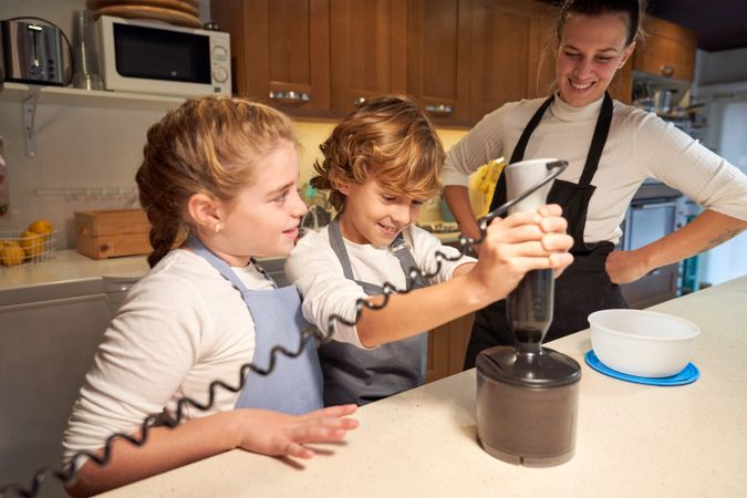Happy children using blender near mother