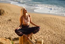 Blonde woman stretching on post overlooking beach with face to the sun