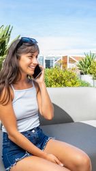 A woman is sitting on a couch and talking on her cell phone. Vertical shot. Copy space