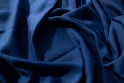 Navy or dark blue fabric wavy spiral crumpled background texture with copy space in the center.