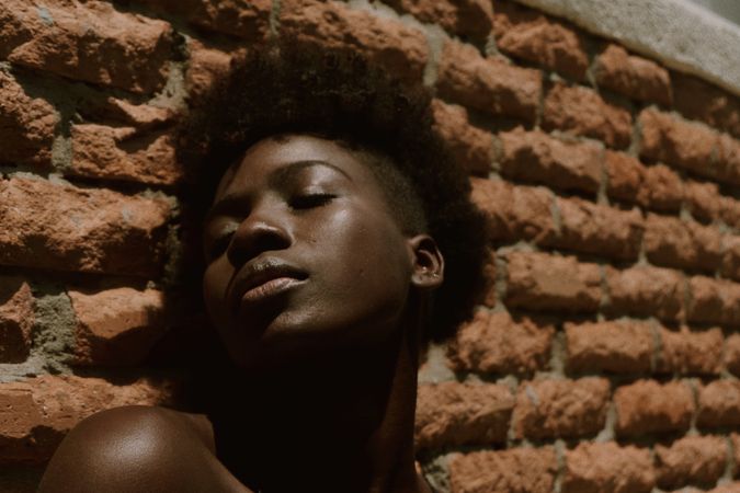 Young Black woman with eyes closed against wall