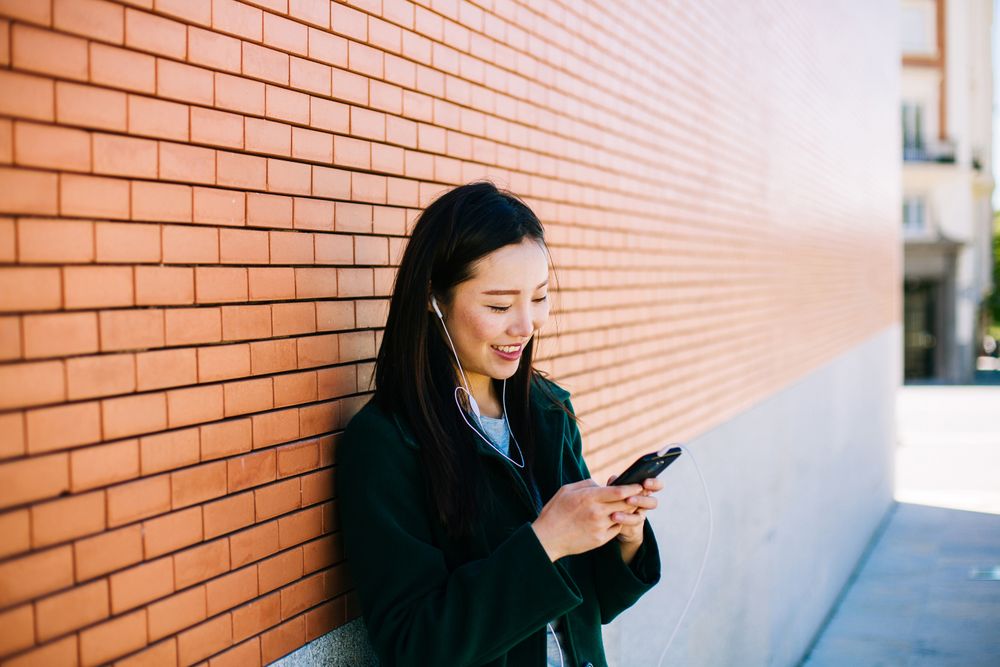 Asian female listening to music near brick wall