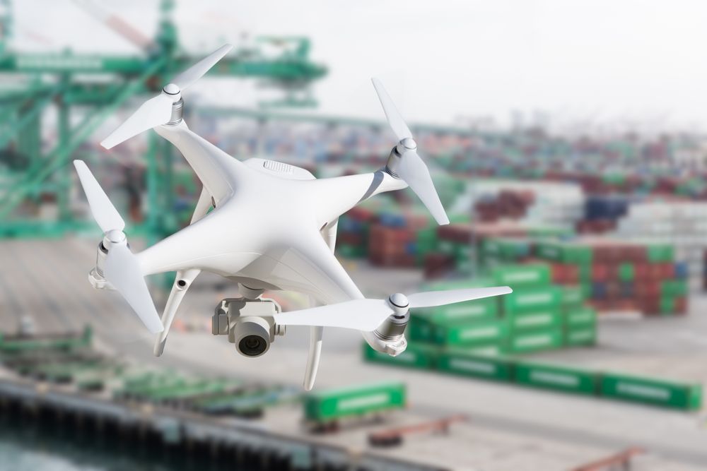 Unmanned Aircraft System Quadcopter Drone In The Air Near Large Shipping Vessel and Dock with Crates