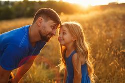 Playful man and daughter  dressed in blue in sunny meadow
