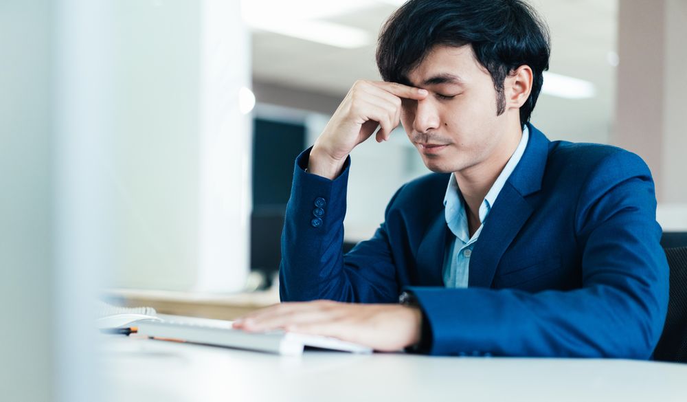 Frustrated Asian male in suit working at computer in his office