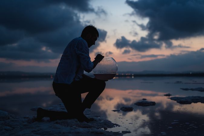 Focused man filling fish tank with water from sea in dusk