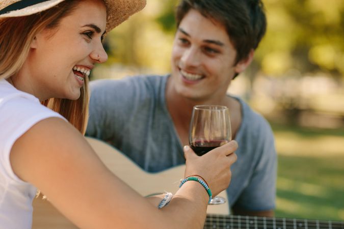 Romantic couple sitting in park drinking wine and playing guitar