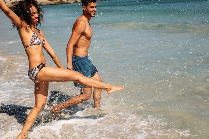 Cheerful woman splashing water with her leg enjoying on the beach