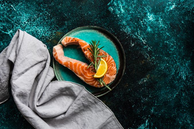Top view of salmon fish with rosemary and lemon on metallic green counter with copy space