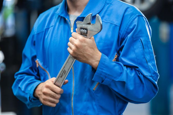 Man in boiler suit holding huge wrench