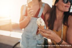 Close up shot of ice cream in hand of a woman standing with her friend 0WXlM5